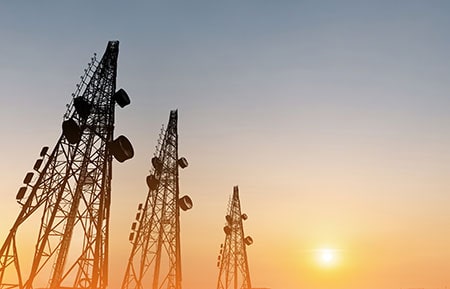 Telecommunication Towers with TV Antennas and Satellite Dish in Sunset